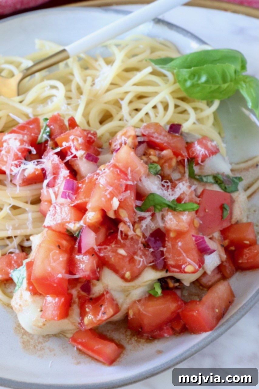 cooked chicken on a plate next to spaghetti noodles covered with tomato bruschetta