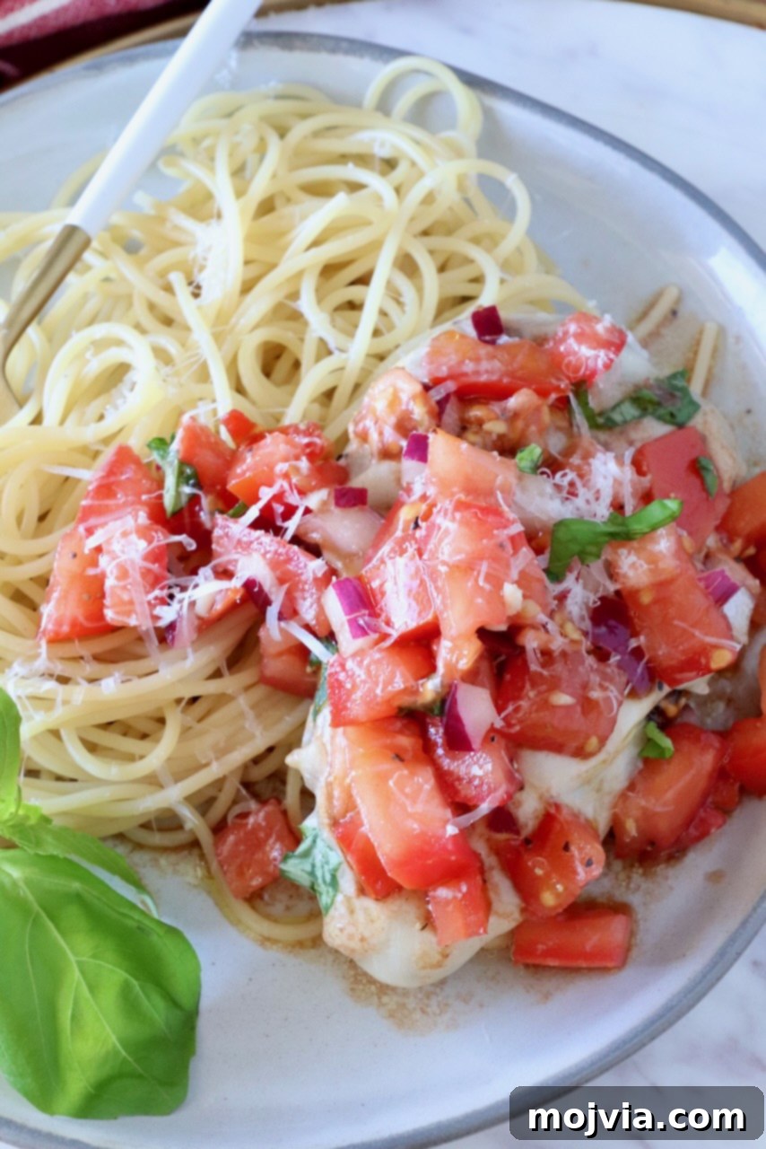 chicken topped with tomato bruschetta on a plate with cooked spaghetti noodles