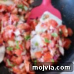 cooked chicken topped with tomato bruschetta in a skillet with a red spatula