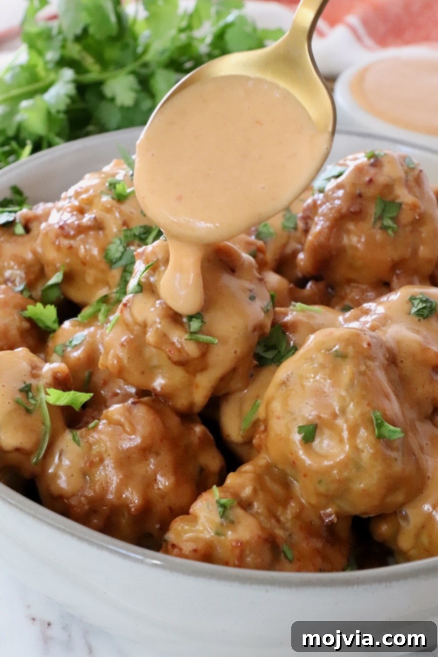 Thai Peanut Turkey Meatball Bliss 2 Thai Turkey Meatballs in a bowl with a spoon drizzling peanut sauce