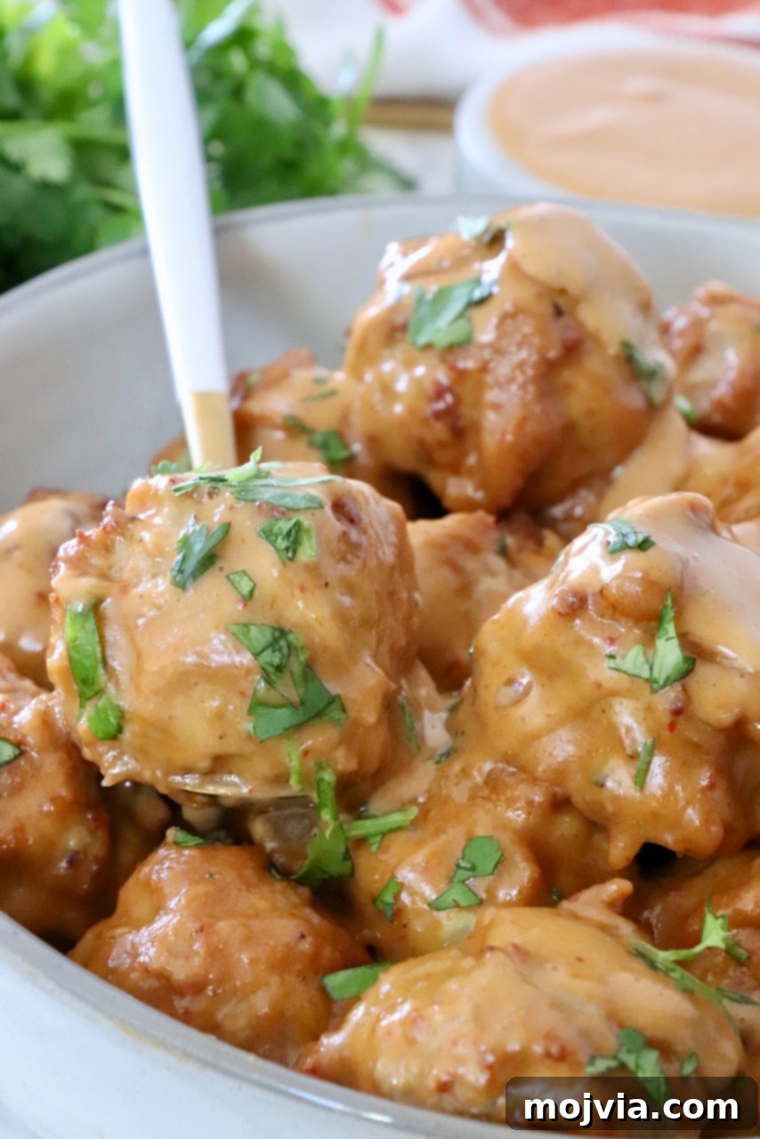 Thai Peanut Turkey Meatball Bliss 10 Close-up of meatballs in a bowl with a spoon, generously covered in peanut sauce