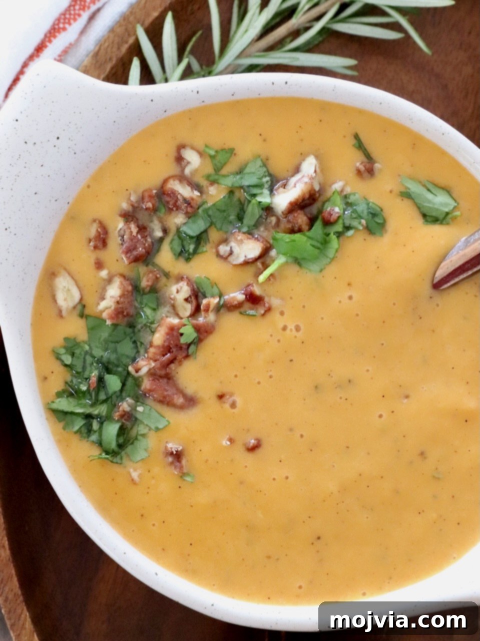 Spiced Sweet Potato Warmth 6 A perfectly garnished bowl of sweet potato soup, topped with chopped pecans and fresh parsley, presented on a light surface.