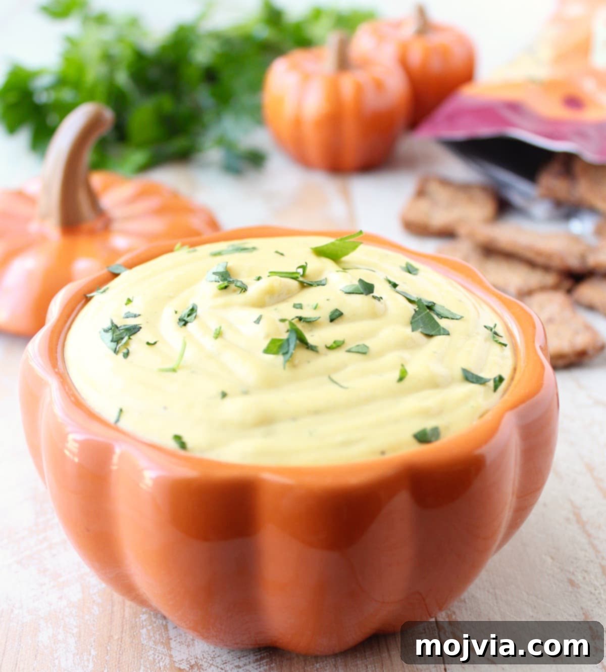 Fiery Pumpkin Harvest Dip 2 Creamy pumpkin dip served in an orange pumpkin-shaped dish, garnished with fresh herbs and surrounded by chips.