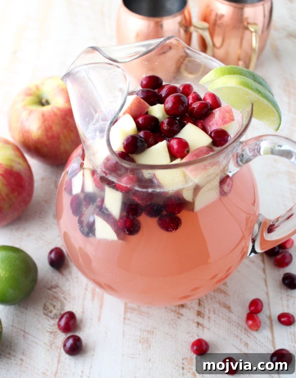 Cranapple Moscow Mule Punch 4 Cranberry Apple Moscow Mule Punch in a large clear glass pitcher, brimming with fresh cranberries and diced apples, ready to be served.