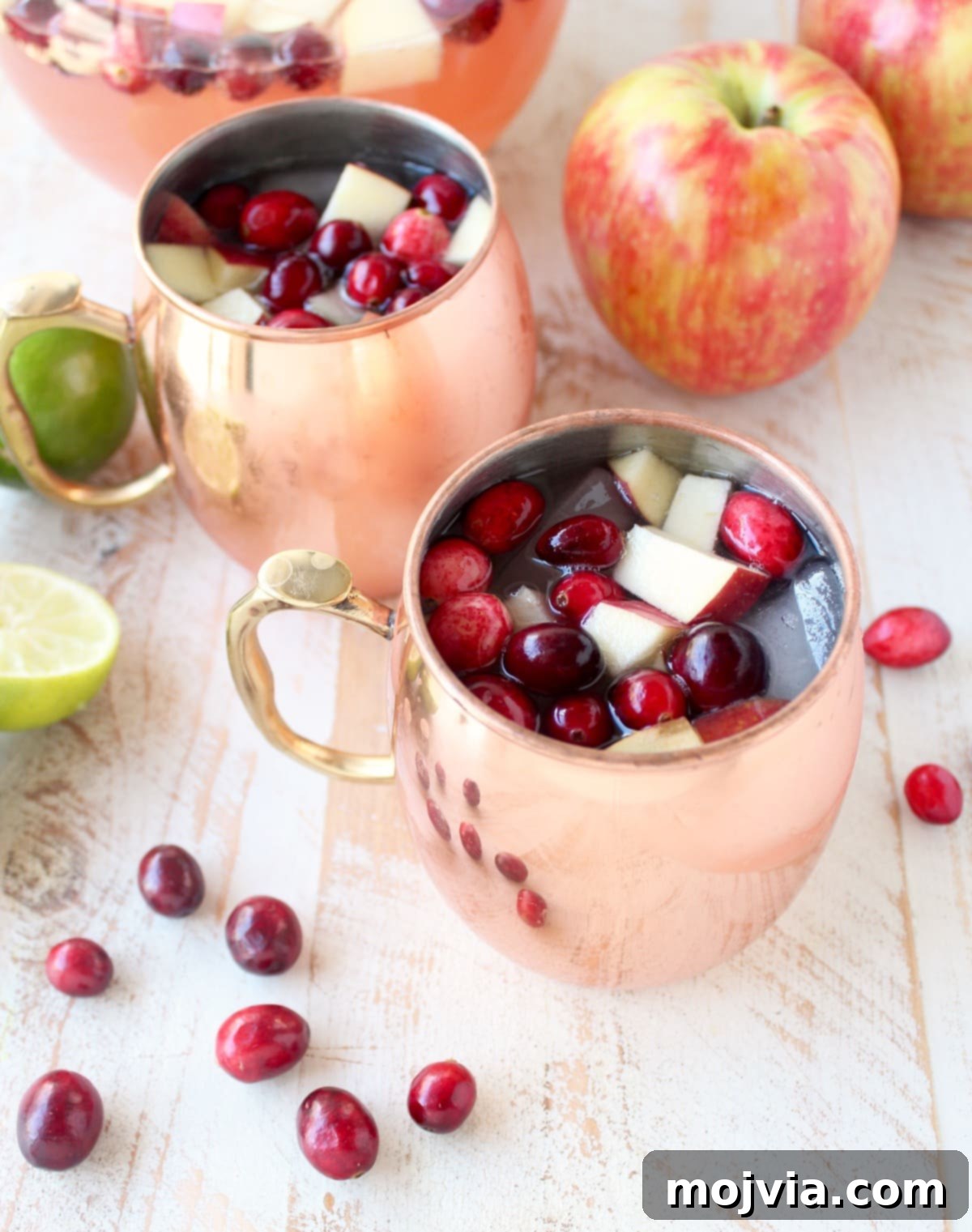 Cranapple Moscow Mule Punch 5 Close-up of Moscow Mule Punch served in traditional copper mugs, beautifully garnished with diced apples and fresh cranberries.