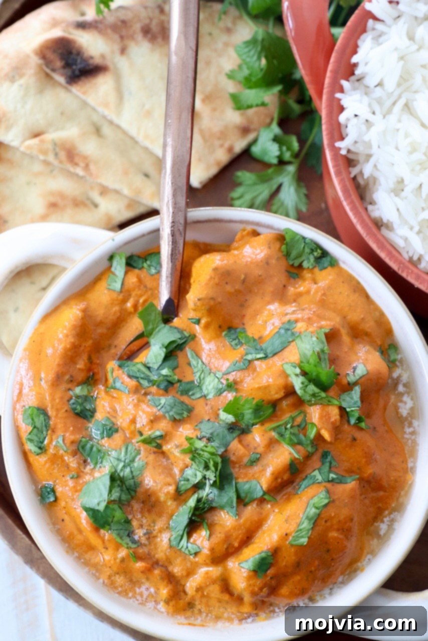 Velvet Butter Chicken 2 prepared butter chicken in bowl with spoon, garnished with fresh cilantro