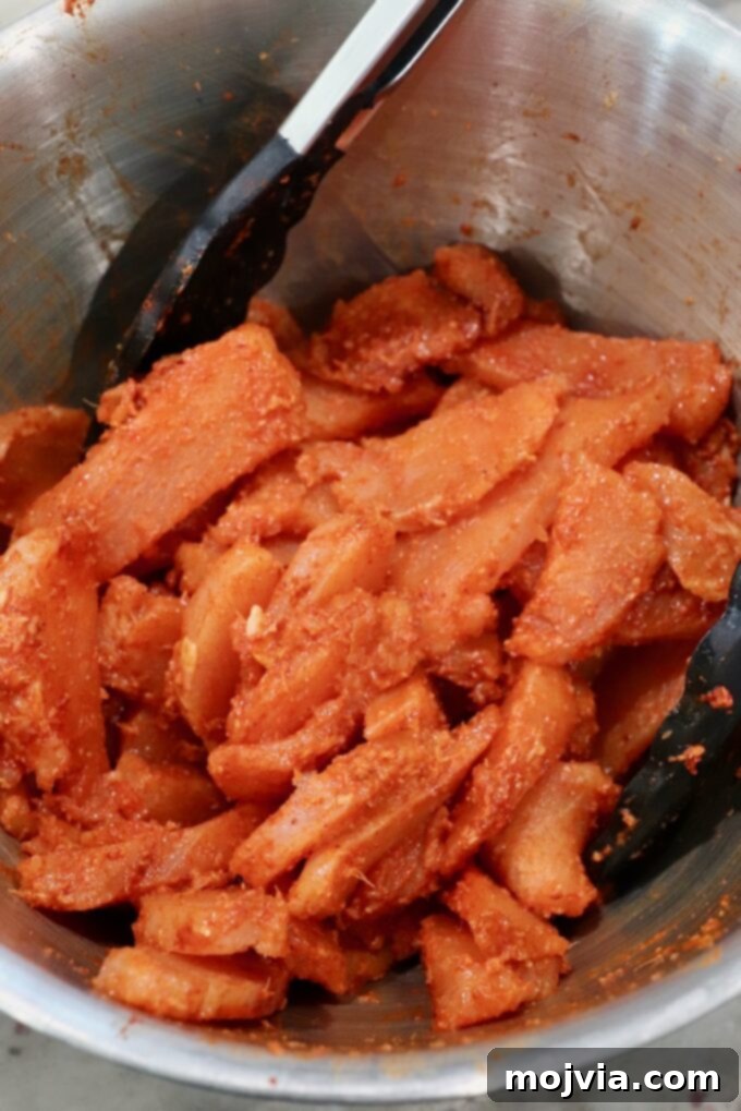 Velvet Butter Chicken 4 strips of raw chicken tossed in spices in metal bowl with kitchen tongs