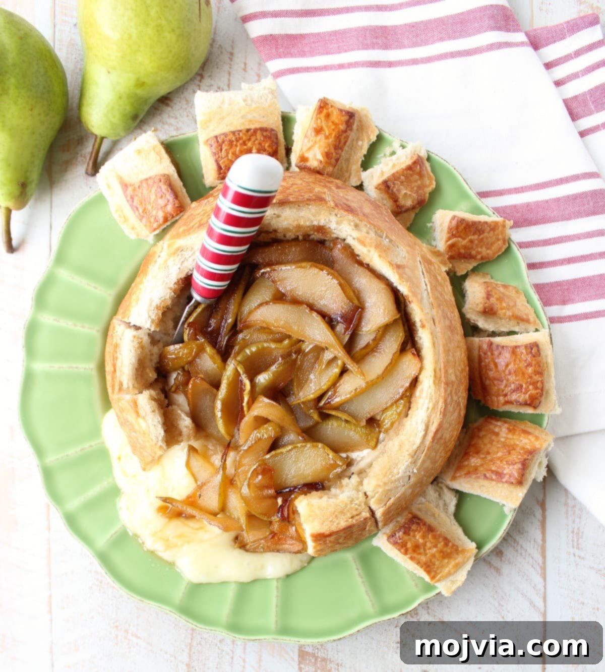 Decadent Caramelized Pear and Brie Bread Bowl 2 Delicious Baked Brie Bread Bowl with caramelized pears and a festive cheese spreader on a green plate, perfect for holiday entertaining.