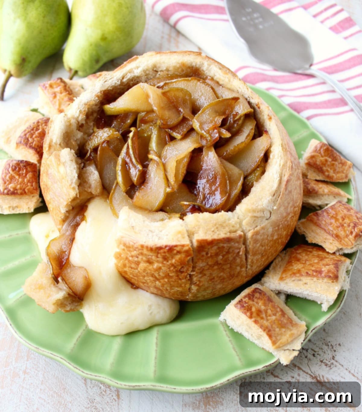 Decadent Caramelized Pear and Brie Bread Bowl 3 Warm, gooey baked brie beautifully spilling out of its sourdough bread bowl, topped with golden caramelized pears on a vibrant green plate.