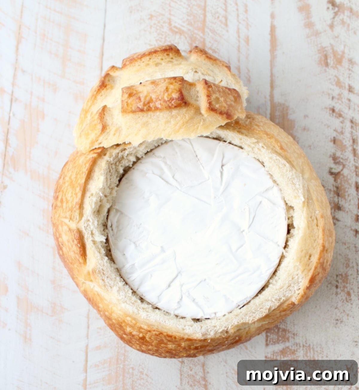 Decadent Caramelized Pear and Brie Bread Bowl 8 A wheel of brie cheese perfectly nestled within the hollowed center of a sourdough bread loaf, ready for the next steps.