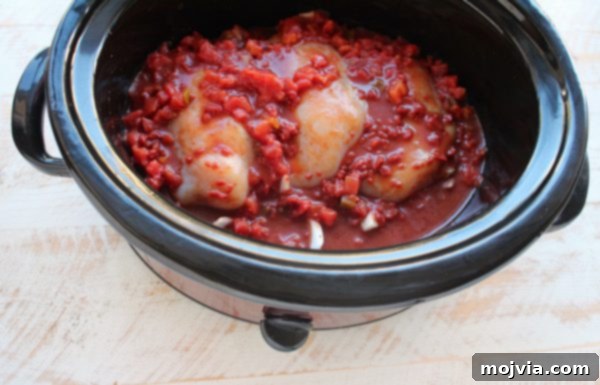 Tender Slow Cooker Chicken Ragu 6 Raw chicken covered in red sauce in a slow cooker.