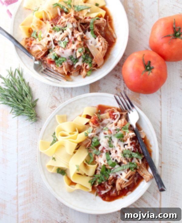 Tender Slow Cooker Chicken Ragu 8 Two white plated topped with pasta, slow cooker chicken ragu, melted cheese, and fresh herbs all on a wooden surface.