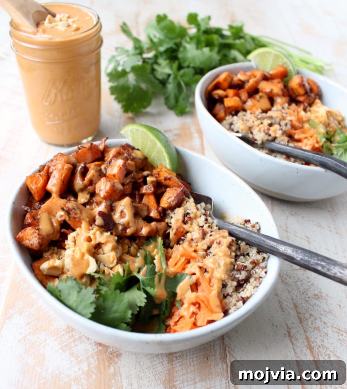 Vibrant Thai Peanut Sweet Potato Bowl 2 Flavorful roasted sweet potatoes and quinoa in bowls, adorned with shredded carrots and fresh cilantro, waiting for a drizzle of rich Thai peanut sauce.