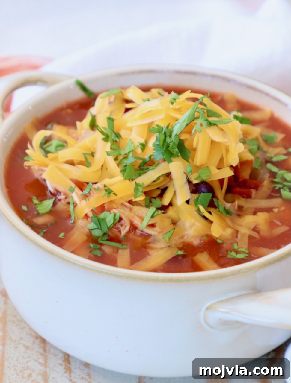 Creamy Chicken Enchilada Crockpot Feast 2 Delicious chicken enchilada soup in a white bowl, generously topped with shredded cheddar cheese, ready to be enjoyed.