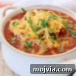 chicken enchilada soup in white crock topped with cheddar cheese