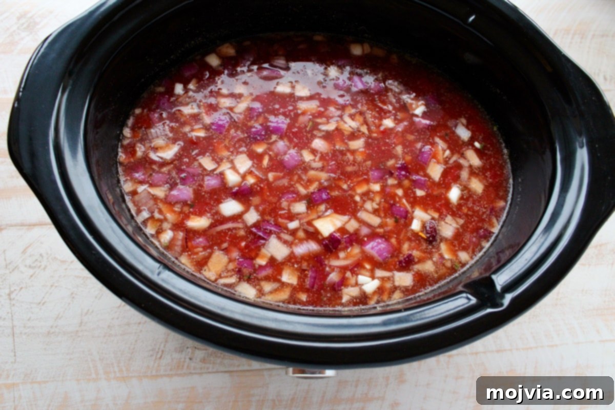 Creamy Chicken Enchilada Crockpot Feast 5 A slow cooker filled with a colorful mixture of chicken broth, diced tomatoes with green chilies, sriracha, tomato paste, diced onions, corn, kidney beans, and black beans, all stirred together.