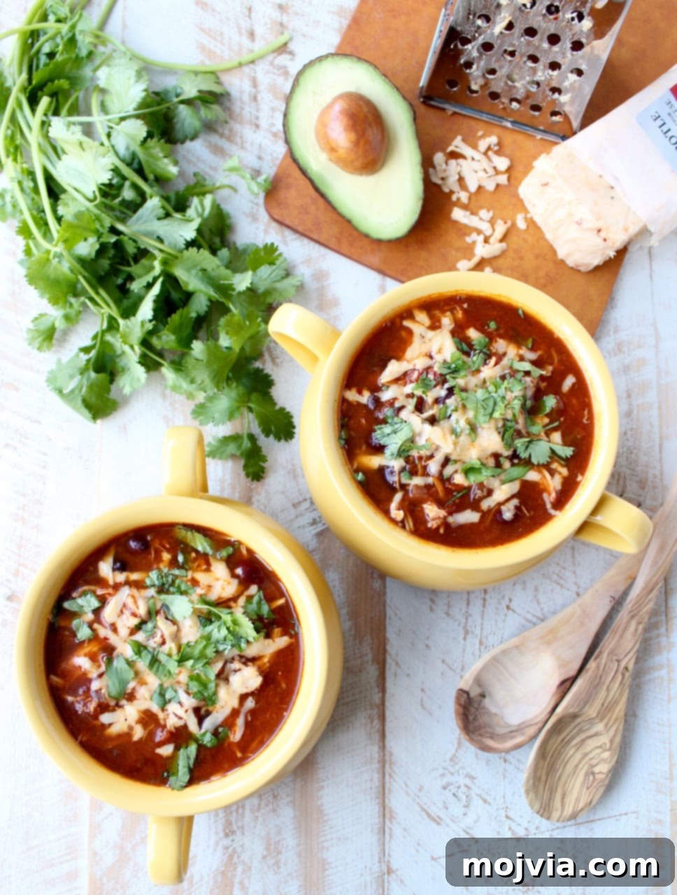 Creamy Chicken Enchilada Crockpot Feast 7 Two cheerful yellow bowls rest on a rustic wooden surface, each brimming with rich enchilada soup, garnished generously with golden shredded cheese and fresh green cilantro, inviting a comforting meal.