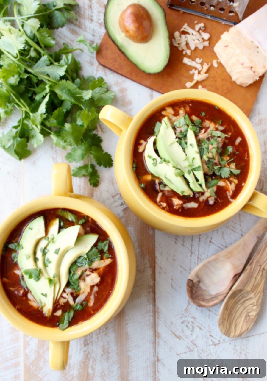 Creamy Chicken Enchilada Crockpot Feast 9 A top-down view of two yellow bowls filled with vibrant enchilada soup, elegantly garnished with fresh sliced avocado and chopped cilantro, highlighting the dish's appealing presentation.