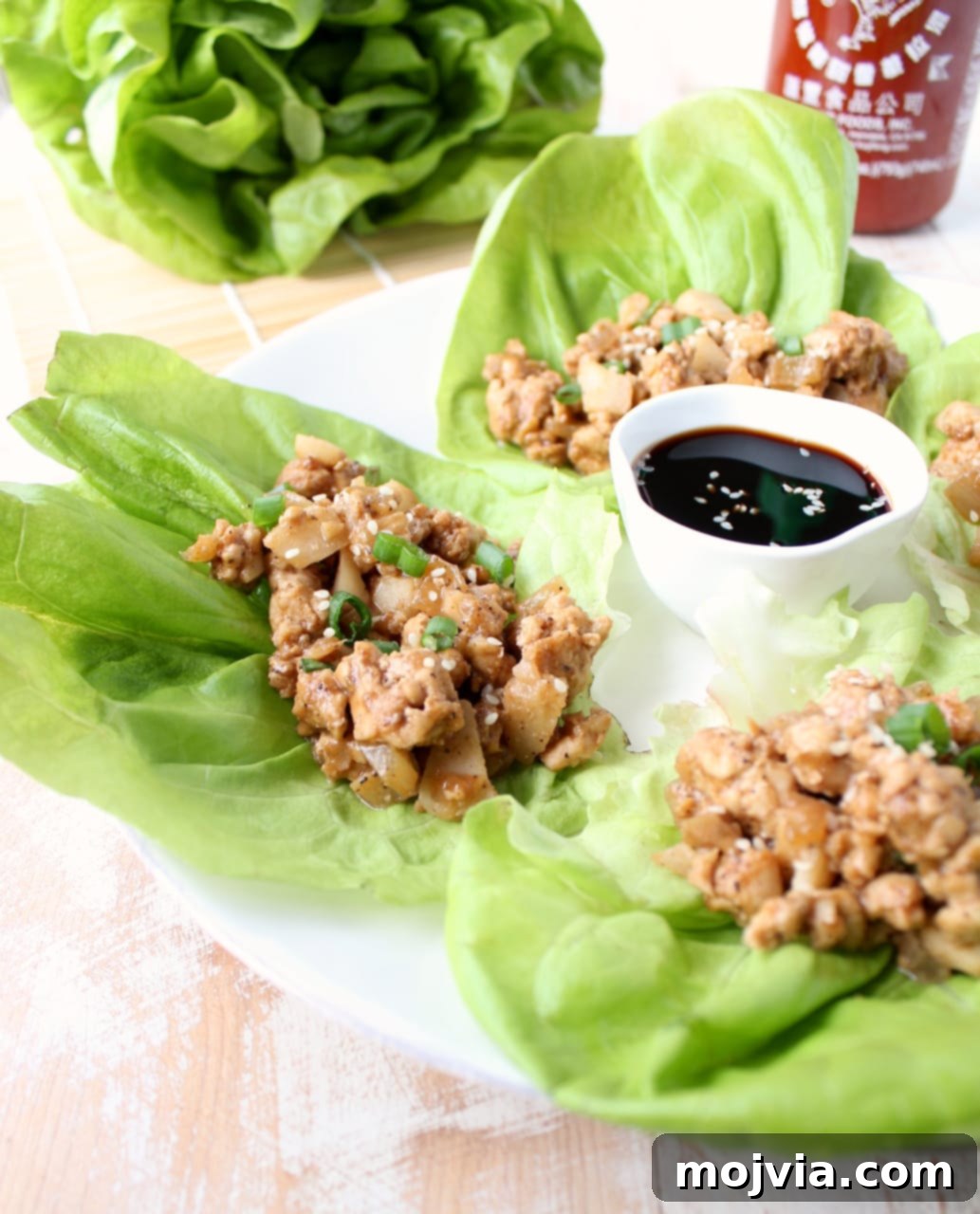 lettuce wraps on a plate filled with a ground turkey mixture with a small bowl of sauce in the middle of the plate