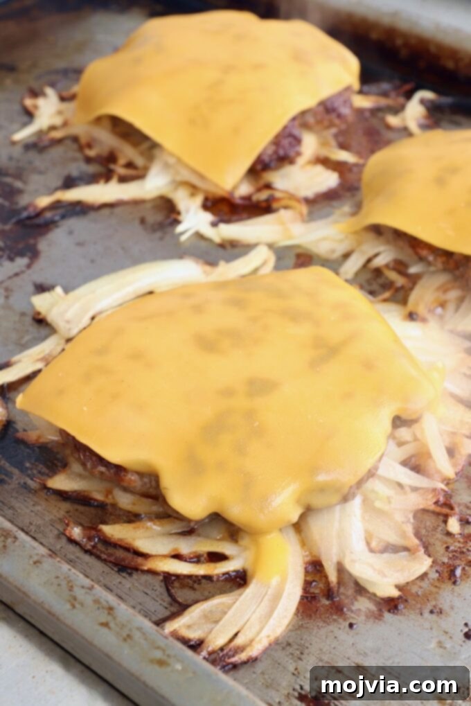 Oklahoma Onion Smash Burger 11 Fried onion burgers on the griddle, now topped with melting cheese, indicating they are almost ready.