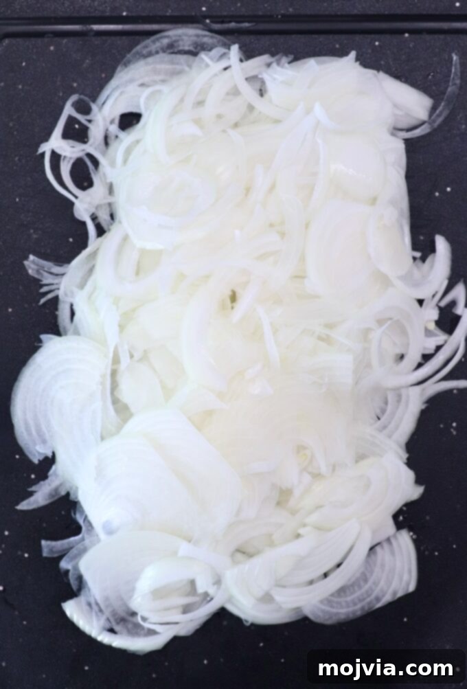 Oklahoma Onion Smash Burger 4 Close-up of thinly sliced yellow onions arranged neatly on a wooden cutting board, ready for preparation.