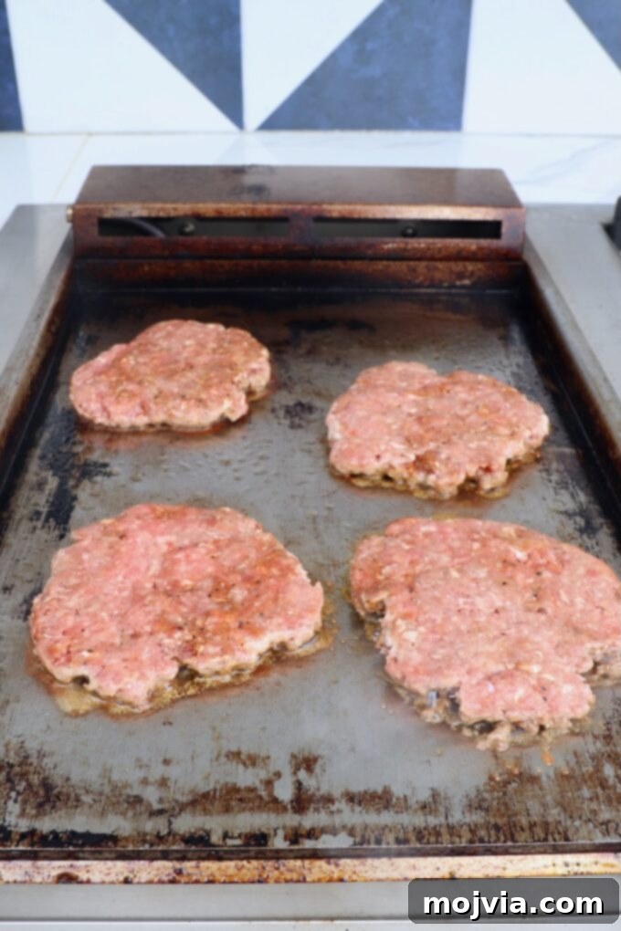 Oklahoma Onion Smash Burger 8 Four perfectly smashed burger patties cooking on a hot griddle, forming a delicious crust.