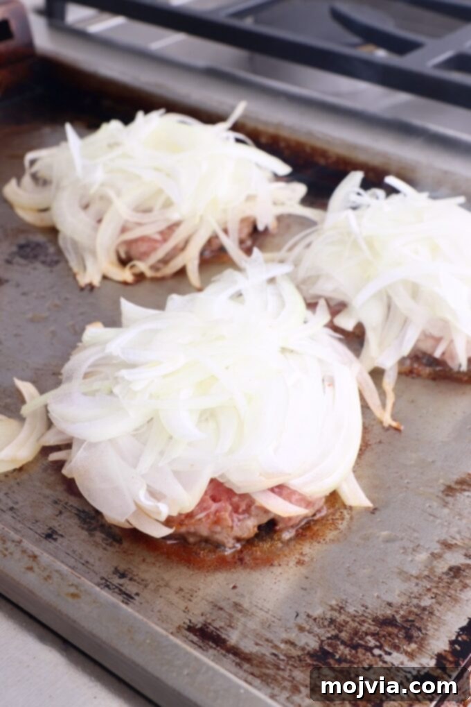 Oklahoma Onion Smash Burger 9 Smashed burger patties on the griddle generously topped with a mound of thinly sliced onions.