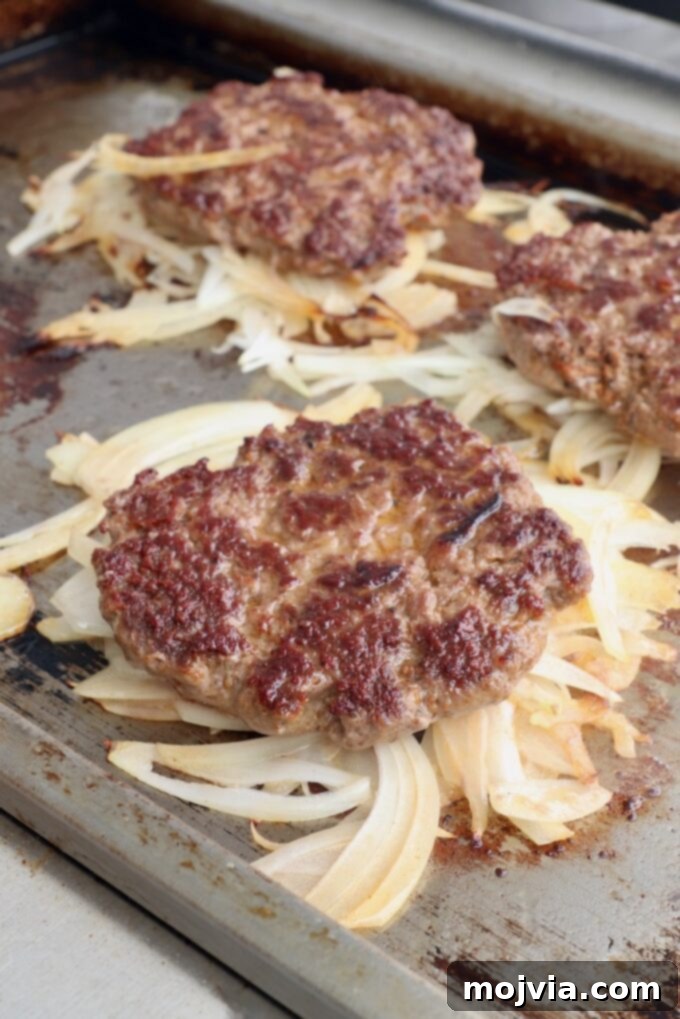Oklahoma Onion Smash Burger 10 Burger patties flipped, now with the grilled onions forming a savory crust on the bottom, continuing to cook on the griddle.