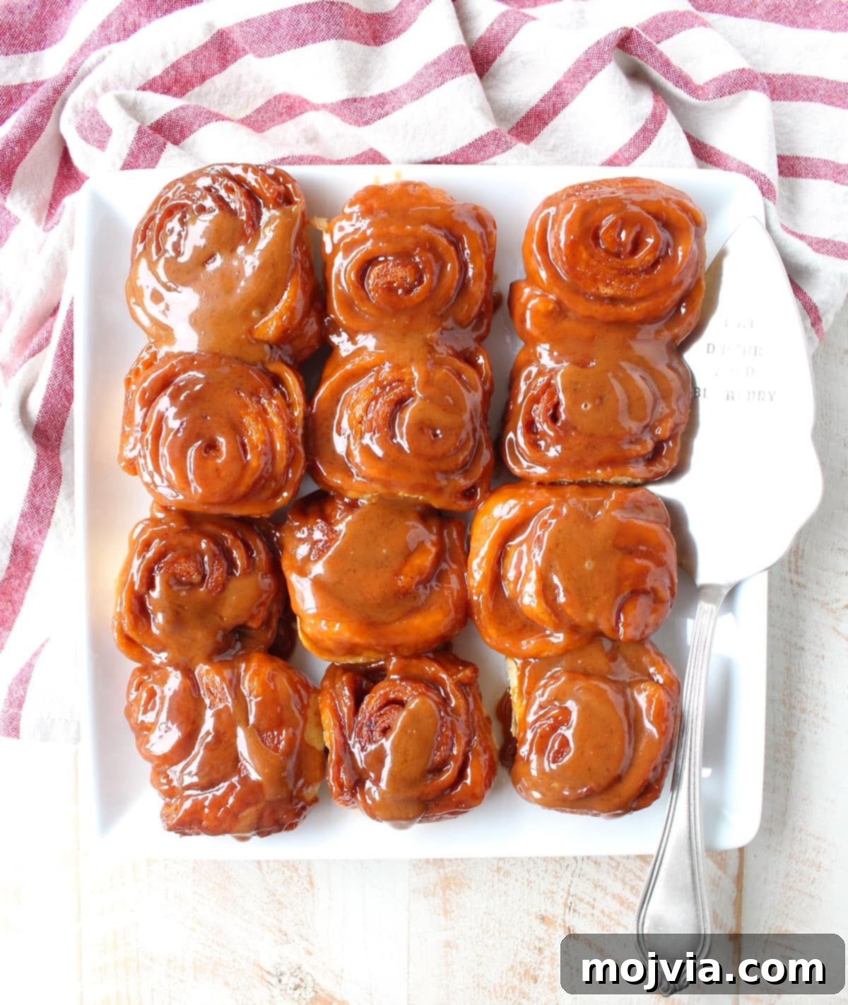 Freshly baked Salted Caramel Cinnamon Rolls arranged neatly on a serving plate, being gently scooped with a pie server, showcasing their readiness to be enjoyed.