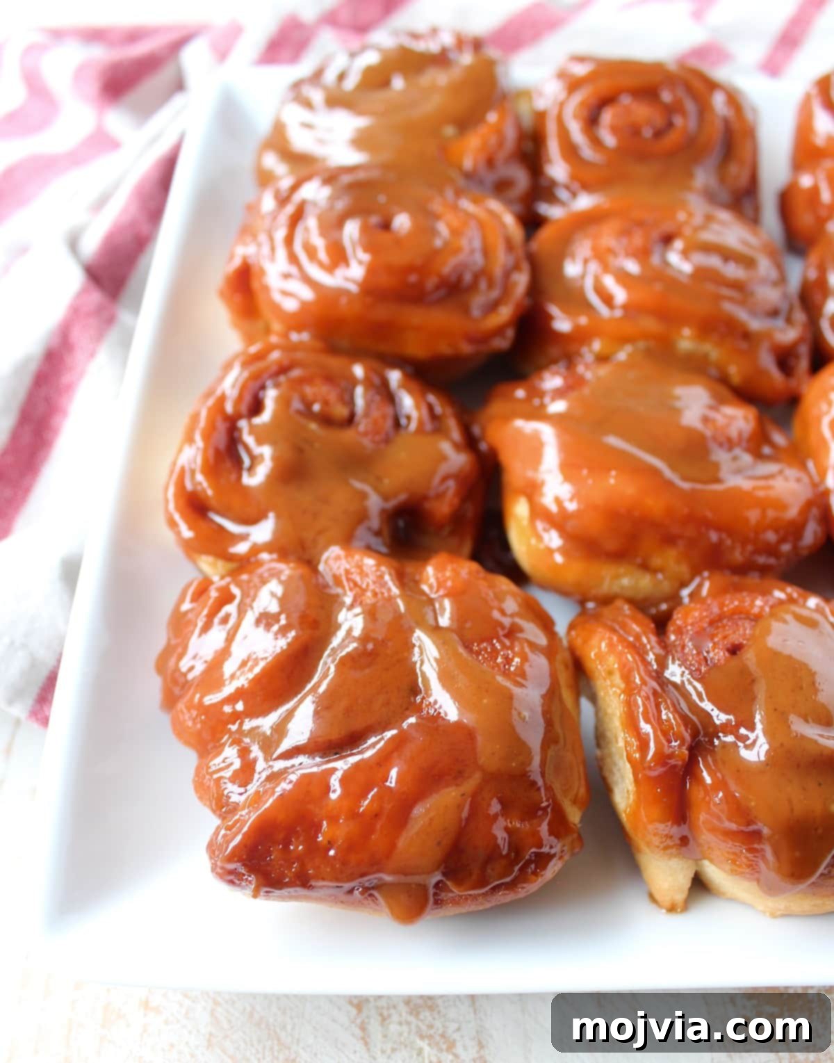 A cluster of beautifully baked Salted Caramel Cinnamon Rolls on a white plate, glistening with their caramel topping, tempting viewers to take a bite.