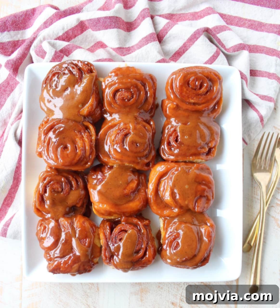 Two perfect Salted Caramel Cinnamon Rolls glistening with caramel, presented on a white square plate, highlighting their irresistible texture.
