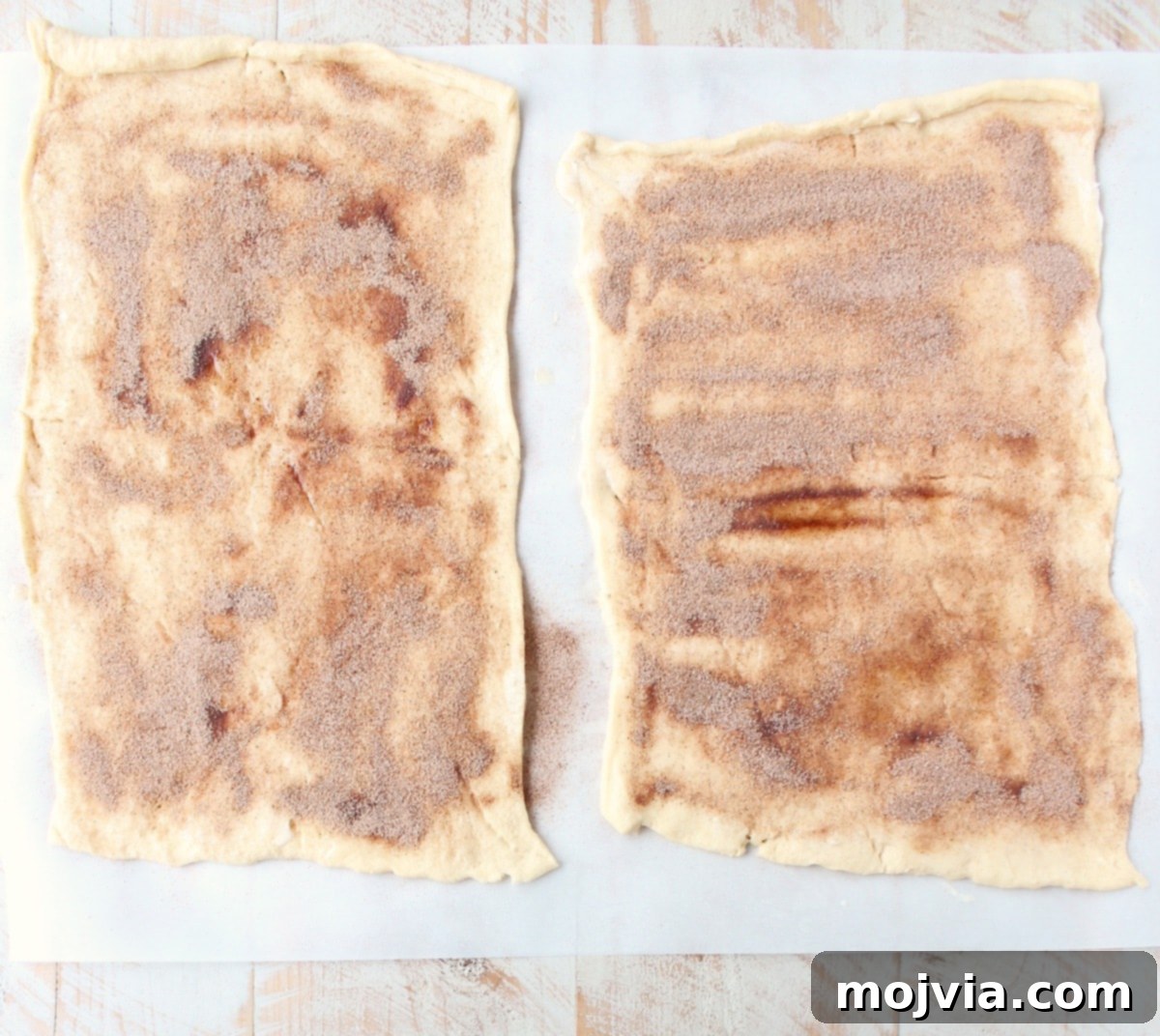 Crescent roll dough spread flat on parchment paper, evenly coated with melted butter and sprinkled with a mixture of cinnamon and sugar.