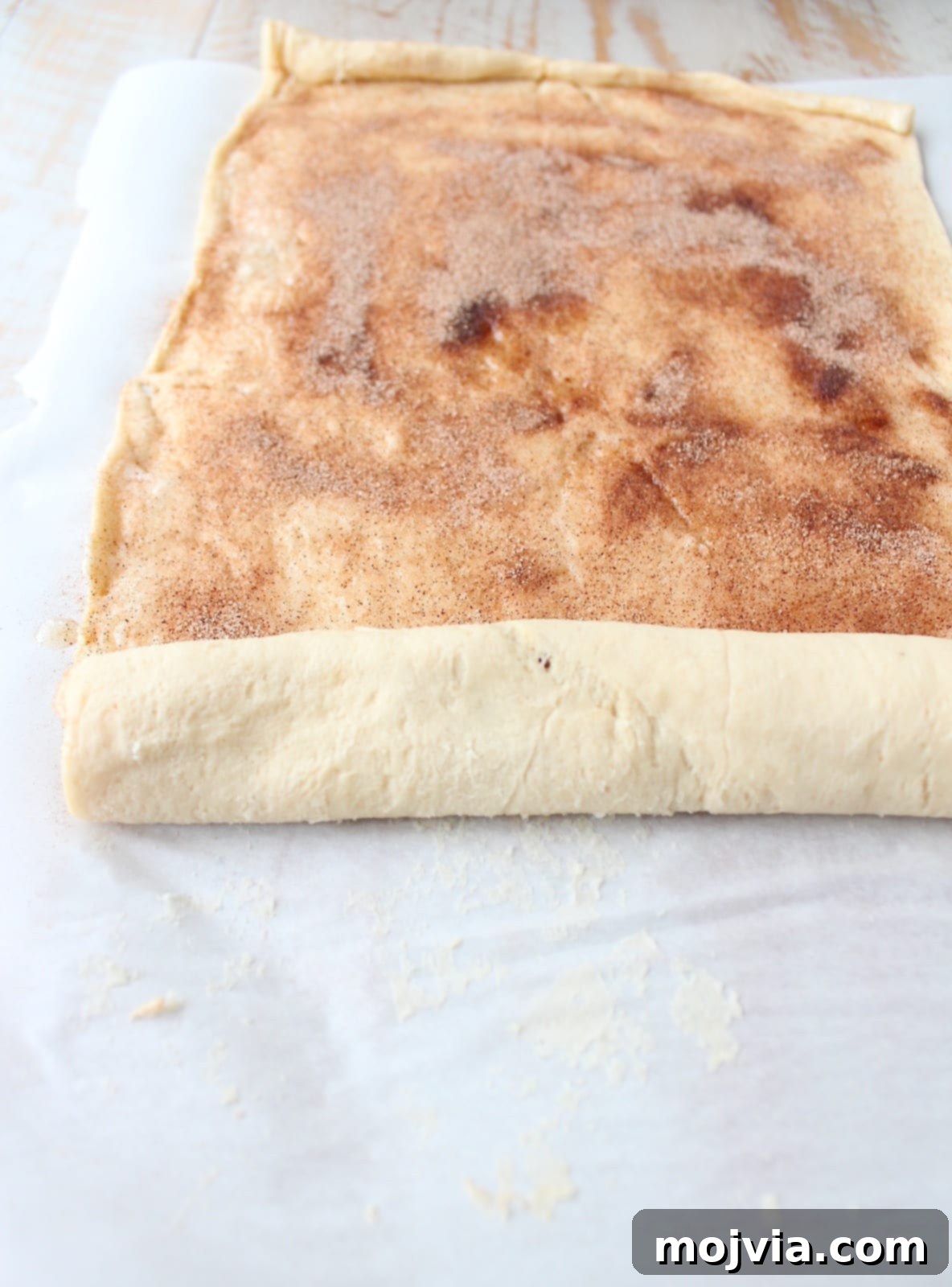 Crescent roll dough rolled up tightly into a log, showcasing the visible layers of cinnamon sugar, ready for slicing.