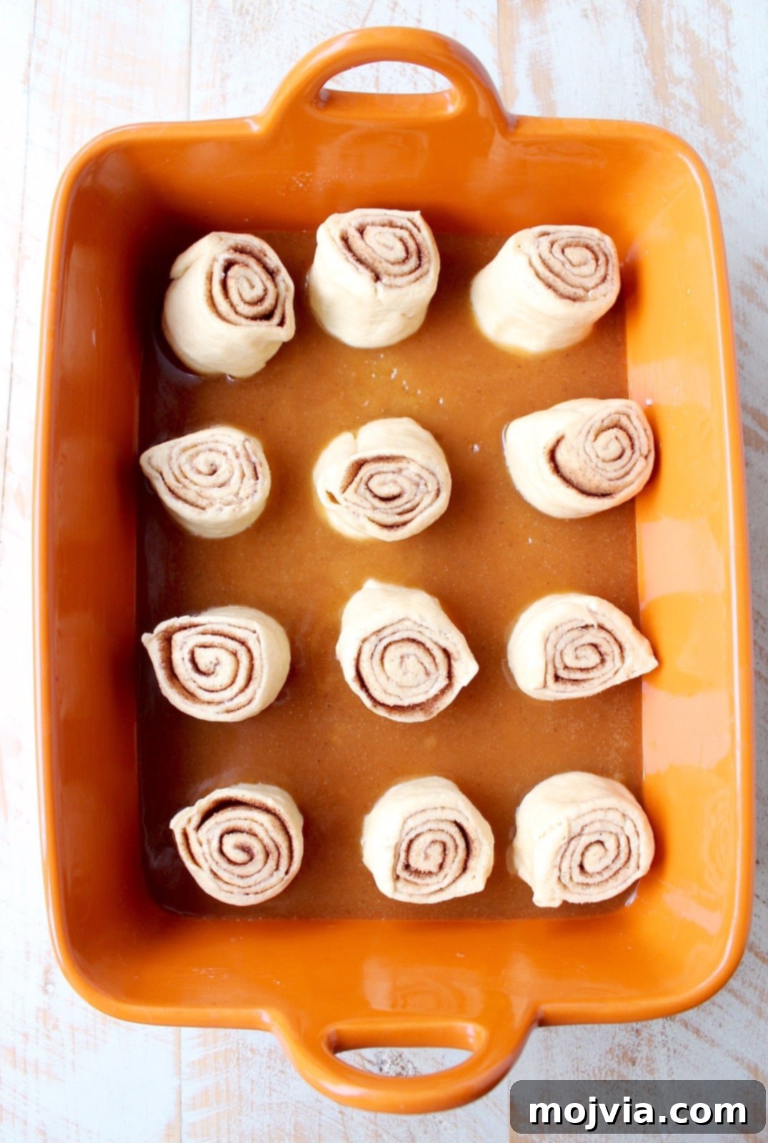 Unbaked cinnamon rolls arranged in a baking dish, nestled on a bed of salted caramel sauce, ready for the oven.