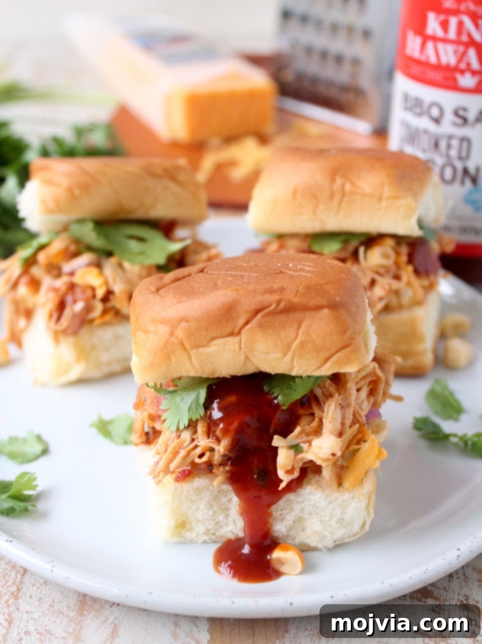 Sweet & Smoky BBQ Chicken Salad Sliders 5 An overhead shot of BBQ Chicken Salad Sliders on a rustic wooden board, with extra BBQ sauce drizzled on top for added flavor and visual appeal.