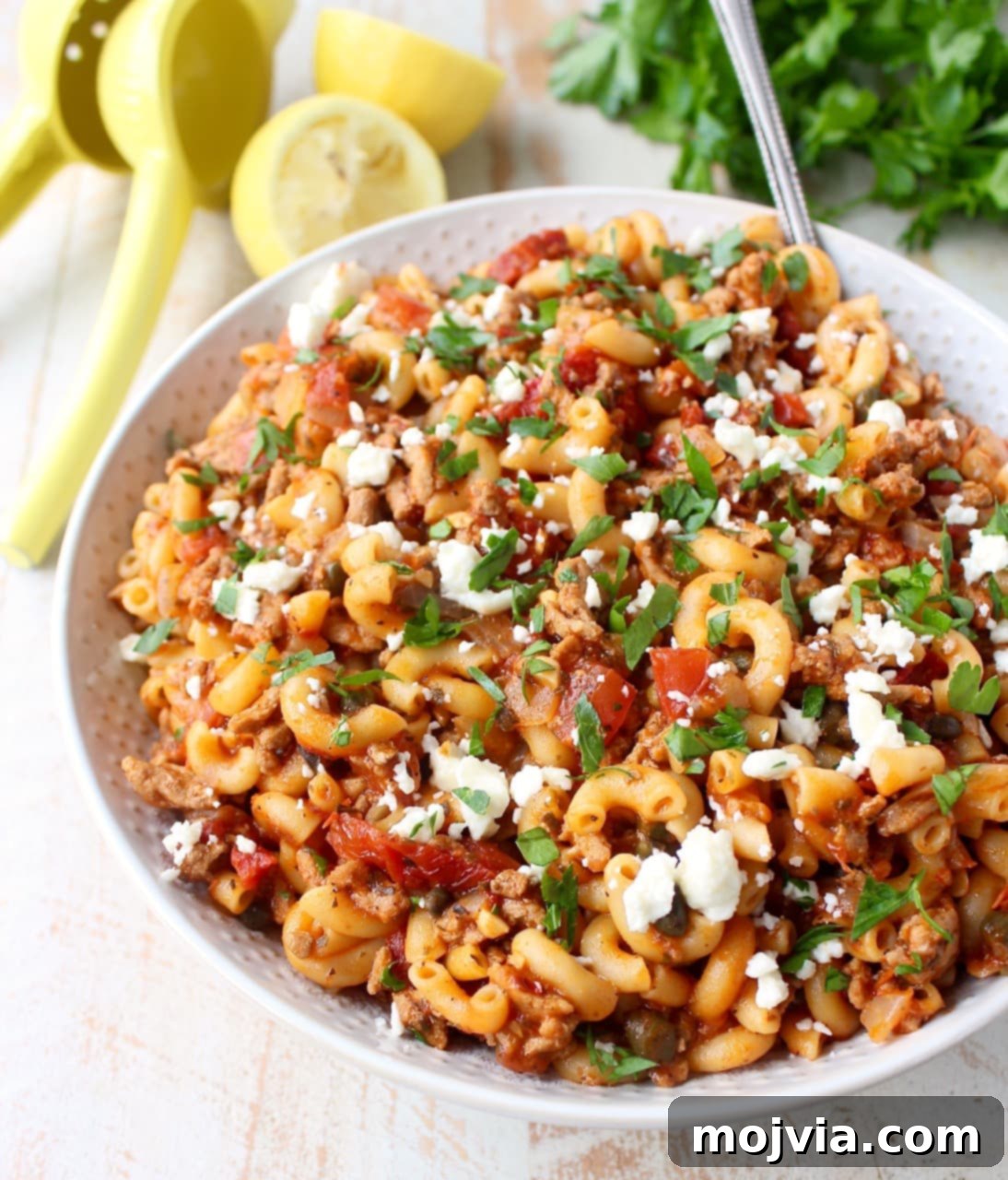 Cooked Greek pasta with ground turkey, diced tomatoes, and crumbled feta cheese in a white serving bowl, garnished with fresh parsley.