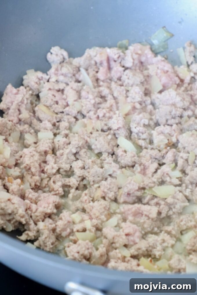 Ground turkey browning in a large skillet with diced onions, ready for seasoning.