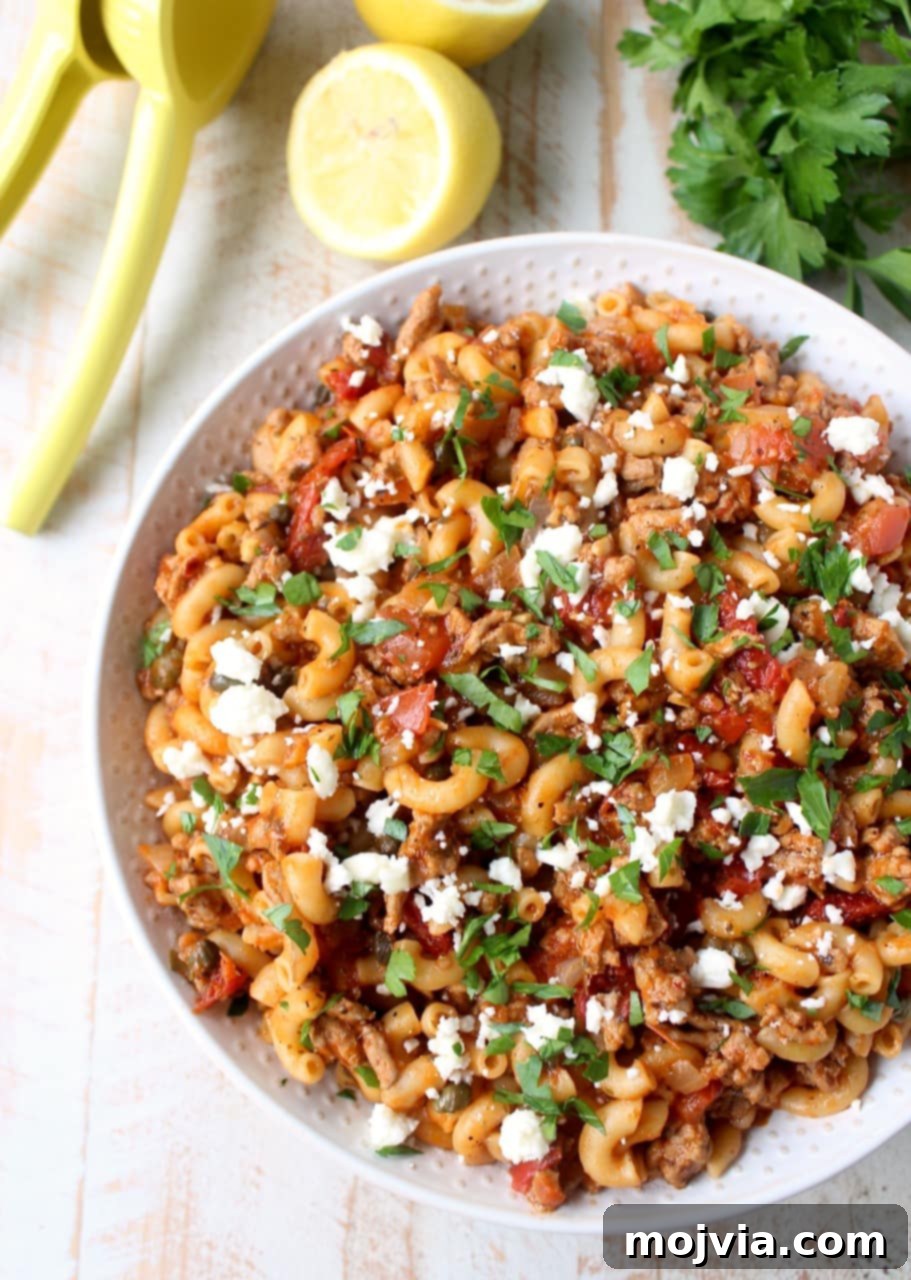 A bowl of freshly prepared One Pot Greek Pasta, topped with crumbled feta cheese and a sprinkle of vibrant fresh chopped parsley, ready to be enjoyed.