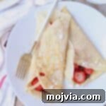 Crepes rolled up on plate filled with nutella and sliced strawberries