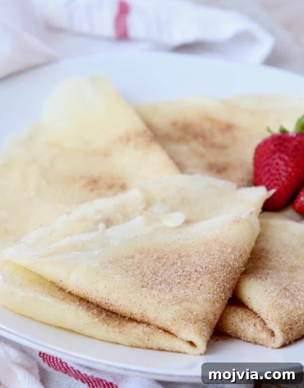 Authentic French Crepes Made Easy 5 cinnamon sugar crepes folded on plate with strawberries