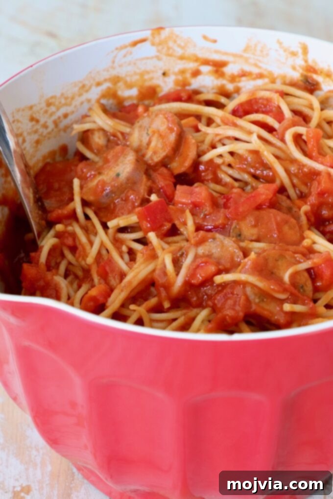 Ultimate Pizza Spaghetti Casserole 4 Cooked spaghetti tossed with rich marinara sauce, sliced Italian sausage, and diced red bell peppers in a large mixing bowl.