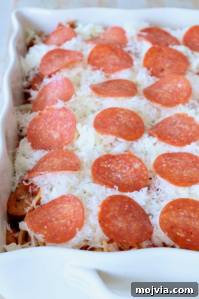 Ultimate Pizza Spaghetti Casserole 7 Spaghetti casserole, now topped with both shredded cheese and an even layer of pepperoni slices, ready for the oven.