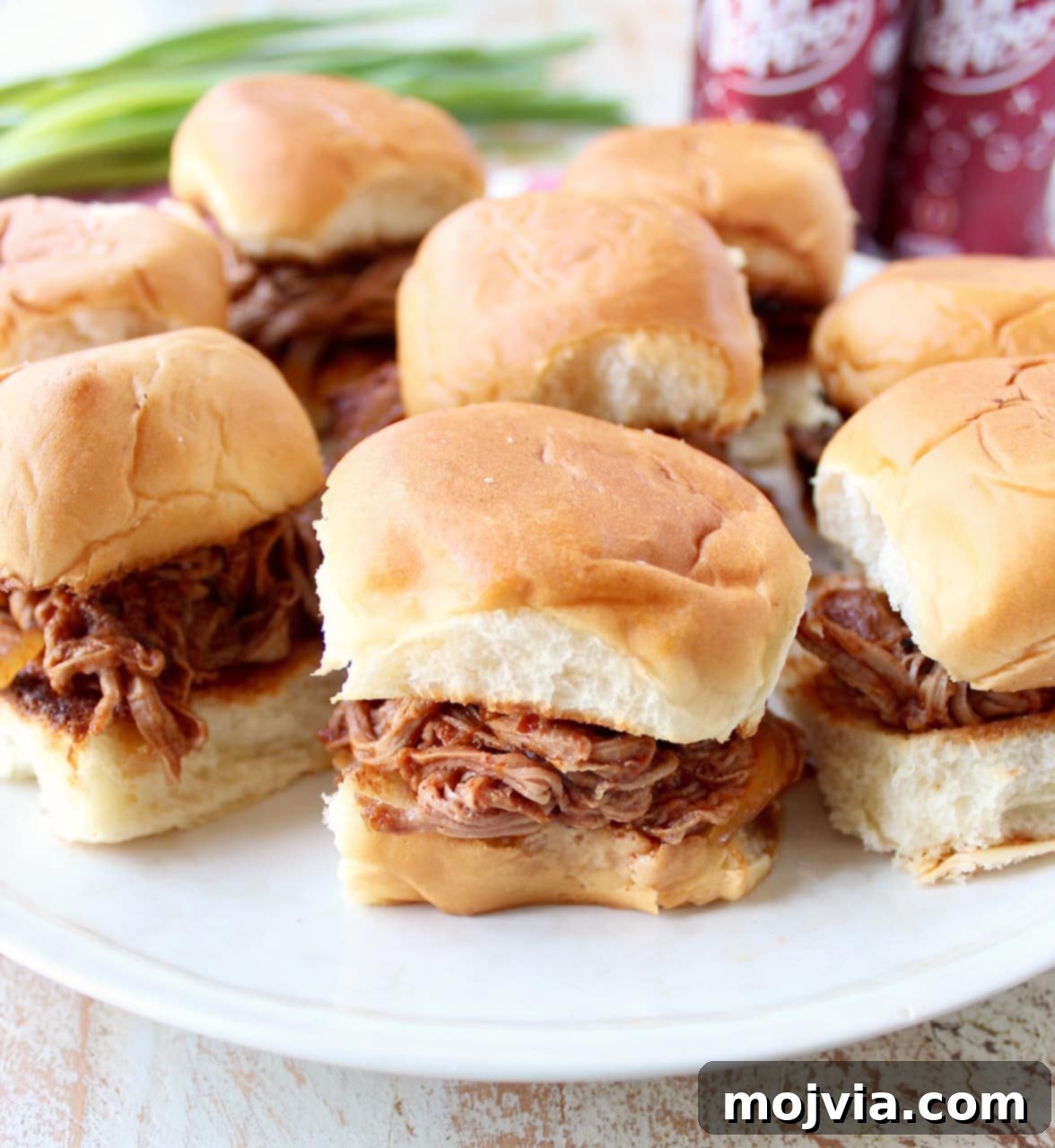 Sweet and Smoky Dr Pepper Pulled Pork Sliders 2 Hawaiian rolls filled with shredded dr pepper pork on a white plate, garnished with fresh herbs.
