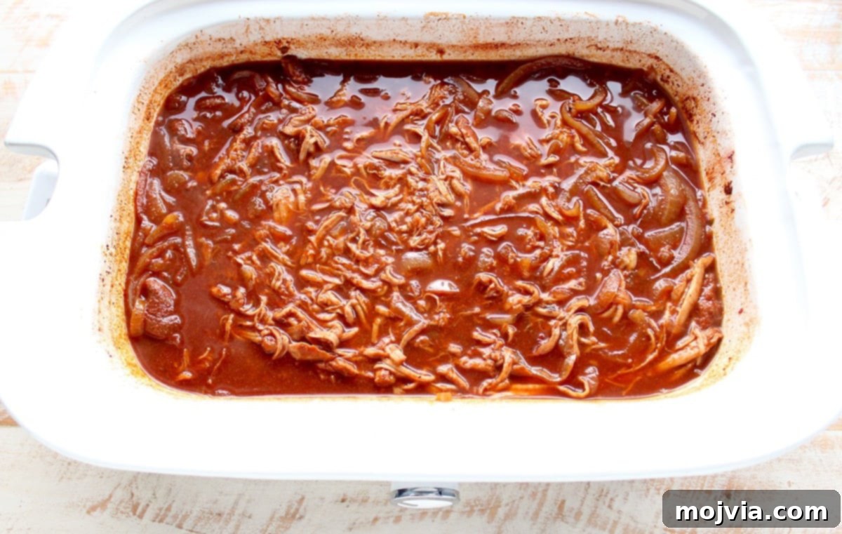 Sweet and Smoky Dr Pepper Pulled Pork Sliders 6 Shredded Dr Pepper pulled pork soaking in its sauce inside a slow cooker.