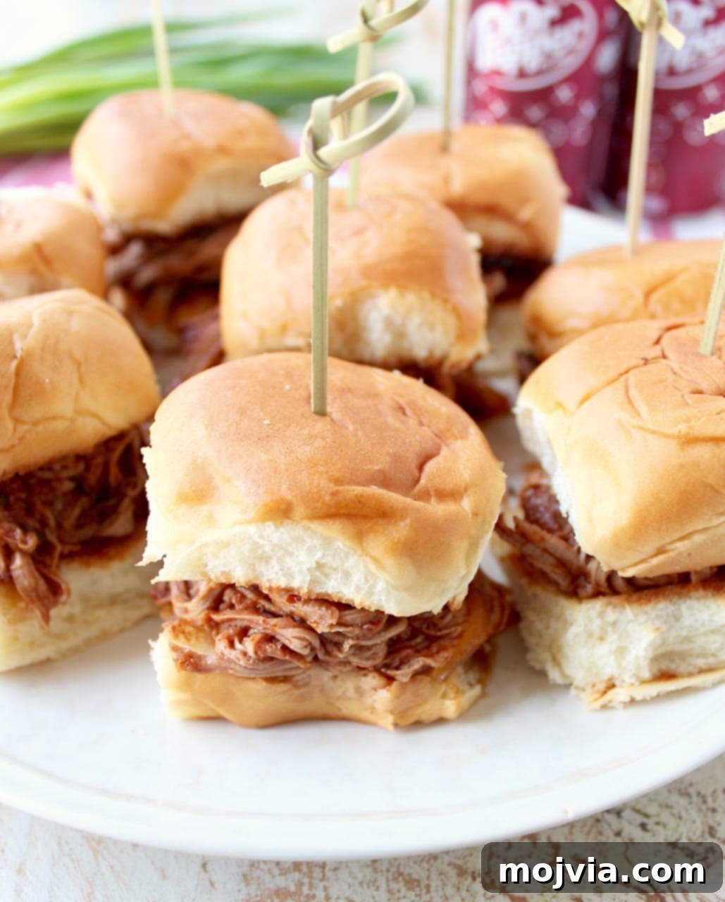 Sweet and Smoky Dr Pepper Pulled Pork Sliders 9 Several Dr Pepper pulled pork sliders on a white plate, garnished with fresh cilantro.