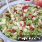 A close-up of the Shaved Brussels Sprout Salad in a bowl, showing the vibrant colors of the sprouts, apples, and pomegranate seeds.