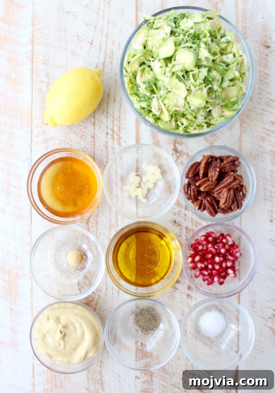 Fresh ingredients for Brussels sprout salad laid out on a white wooden board, including whole Brussels sprouts, a red apple, a pomegranate, pecans, and small bowls of dressing ingredients.