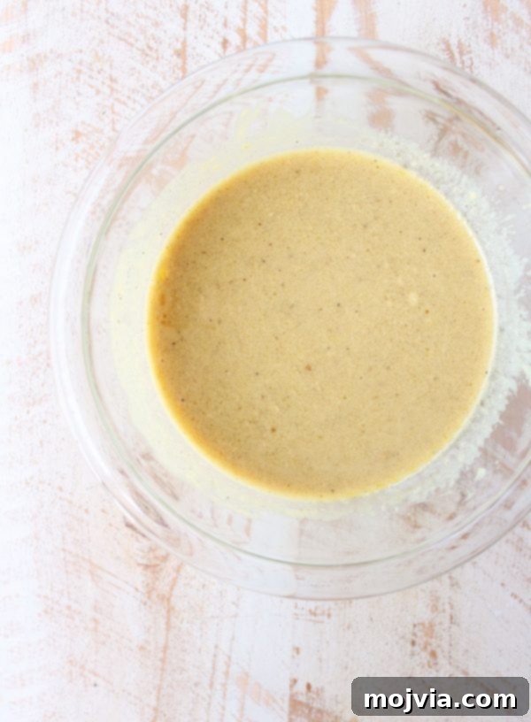 Close-up of a small bowl filled with freshly whisked honey dijon dressing, showcasing its smooth texture and golden hue.