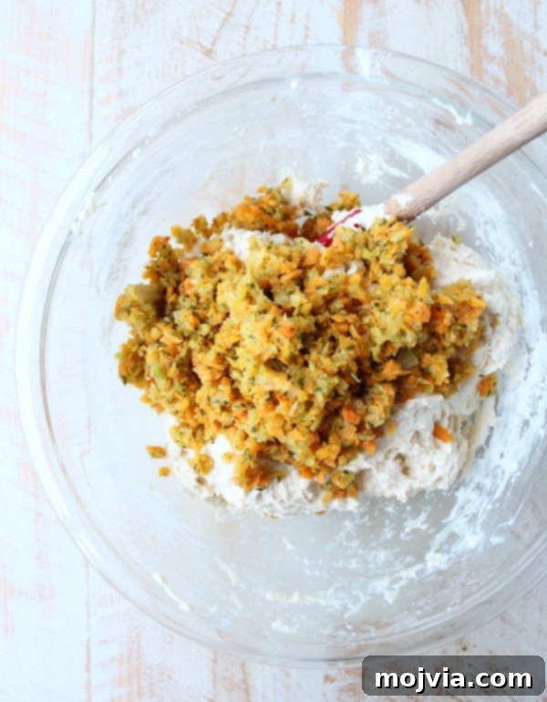 Savory Stuffing Biscuits 5 Biscuit dough being mixed with the sautéed minced vegetables using a spatula in a glass bowl.