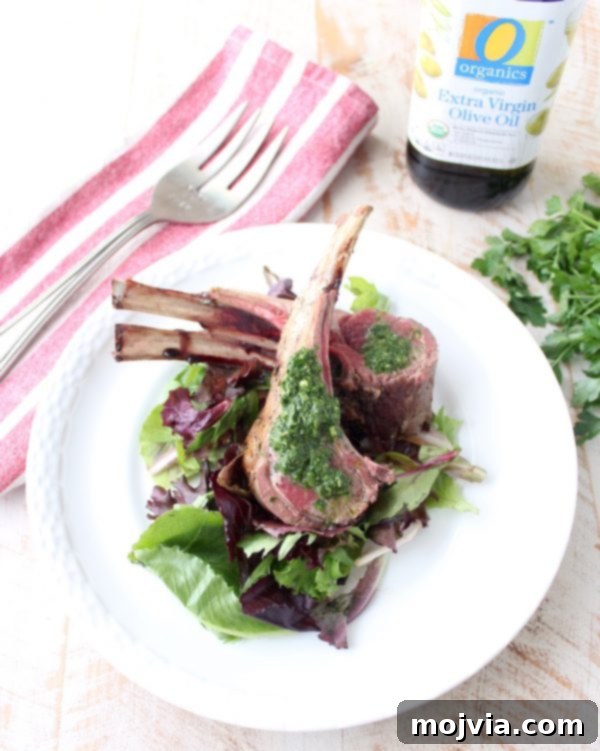 Succulent Herb Butter Roasted Lamb with Vibrant Mint Chimichurri 3 A close-up of a roasted rack of lamb, showcasing its herb crust, with a vibrant mint chimichurri sauce on the side.